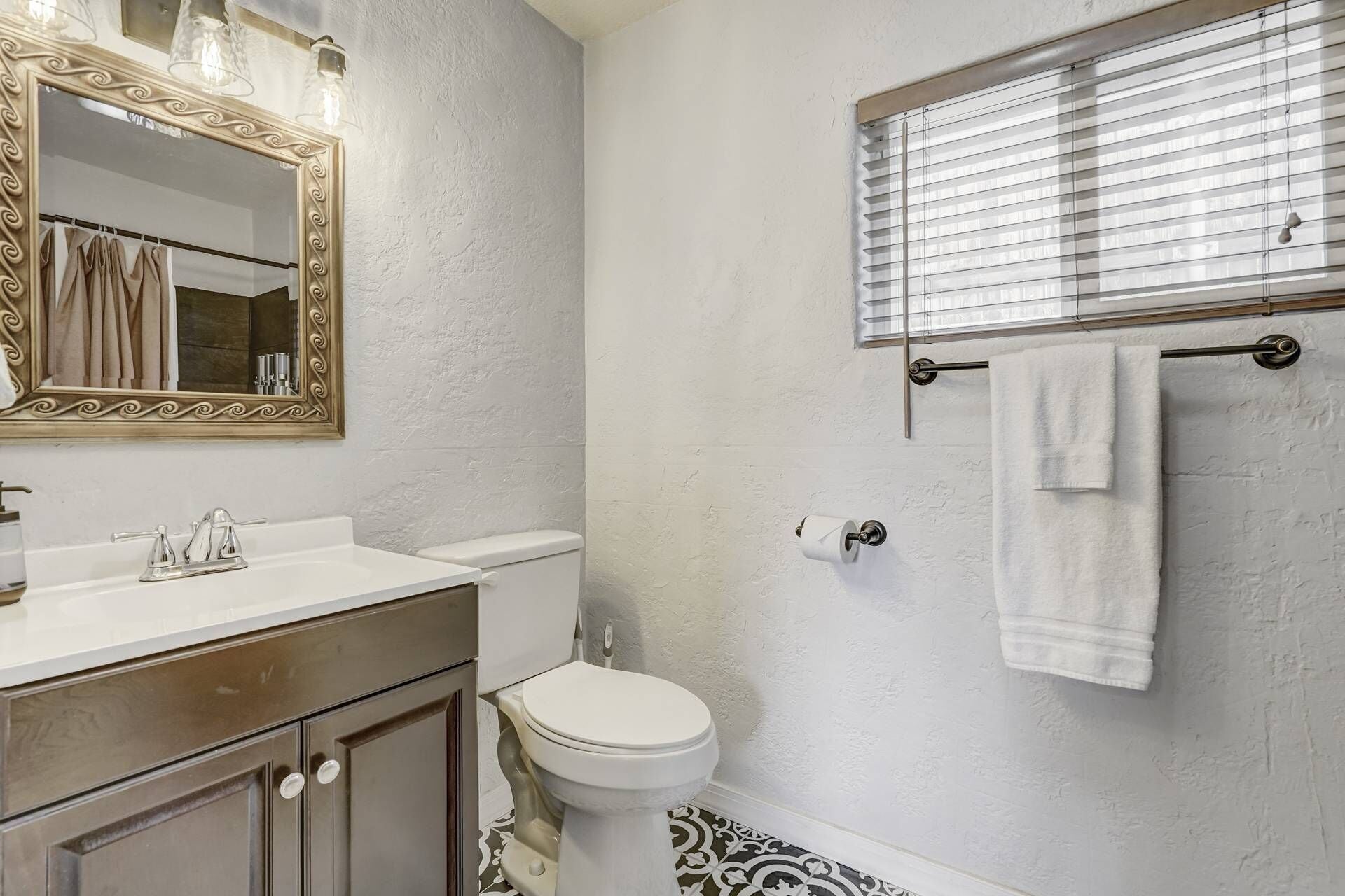 A bathroom with a white sink, a toilet, a mirror with a decorative frame, and a towel rack with a towel.