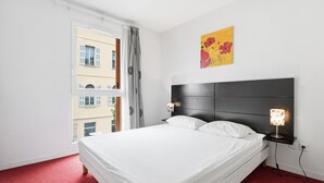 Ein Hotelzimmer mit einem großen Bett, einem Nachttisch mit Lampe, einem Fenster mit Vorhängen und einem Bild an der Wand.