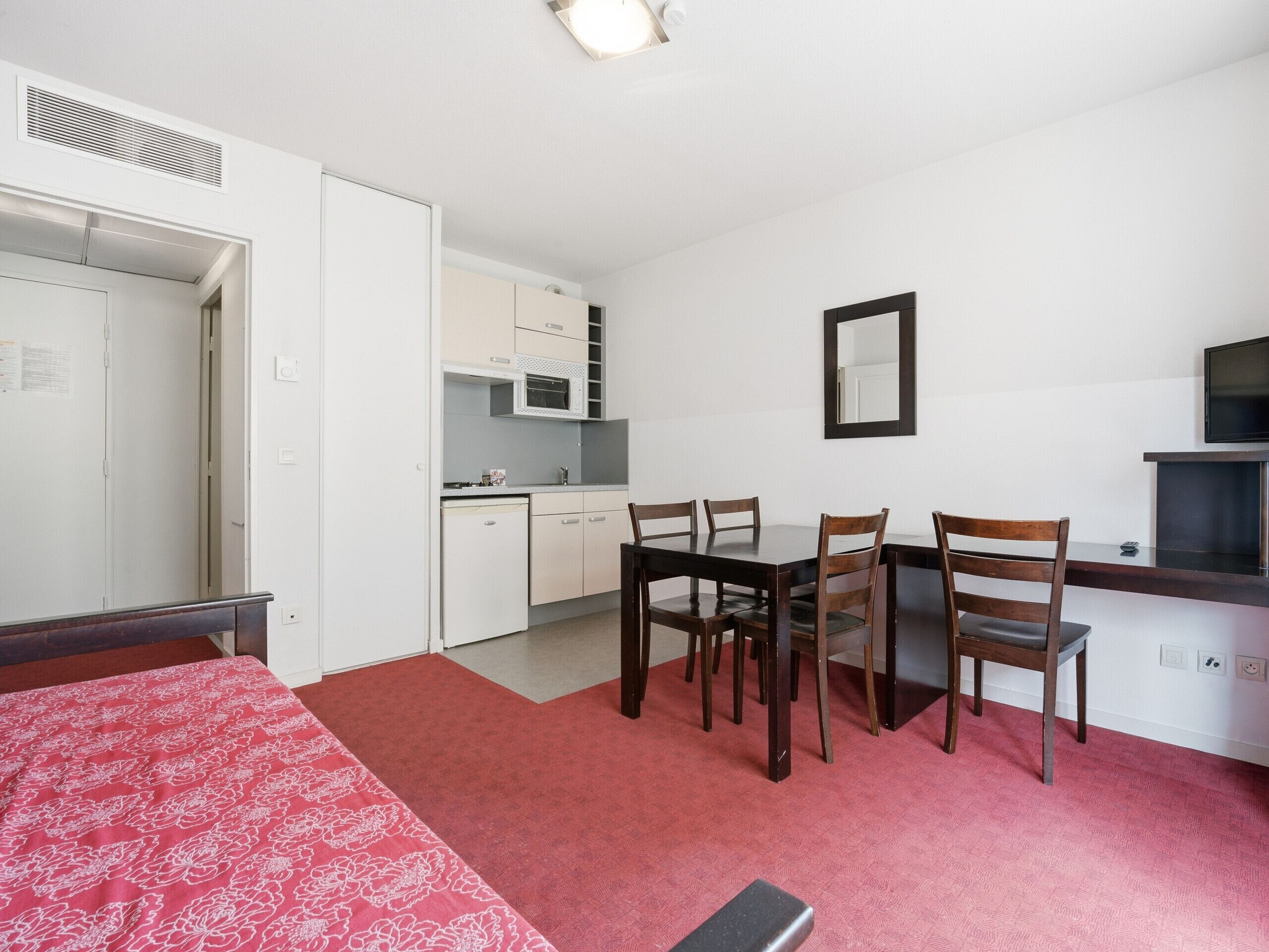 Una habitación compacta con cama, una mesa de comedor con sillas, kitchenette y televisor.