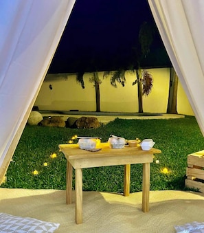 A tent set up on a grassy area with a table in front, surrounded by rocks and palm trees.