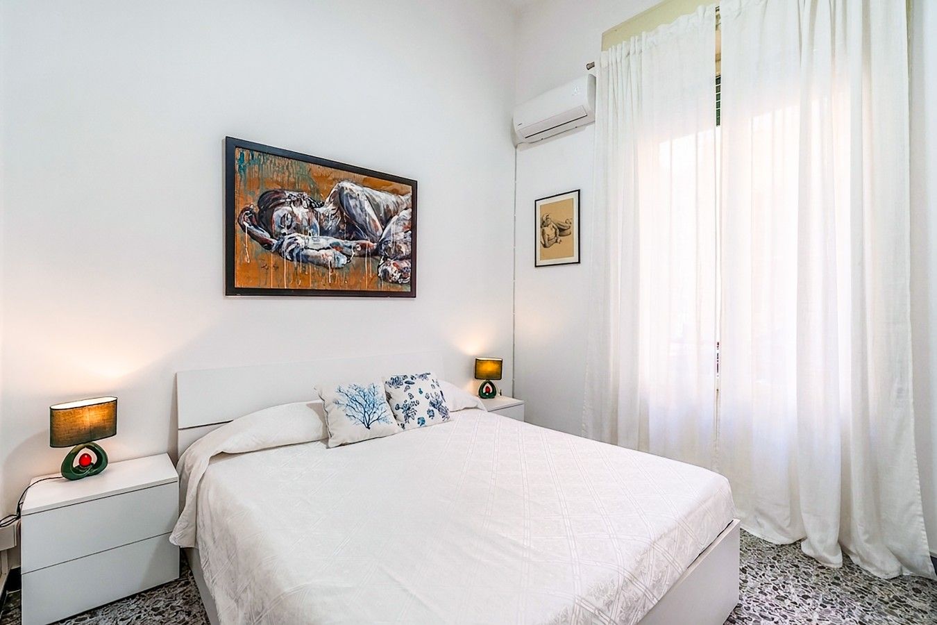 Une chambre à coucher avec un lit, deux tables de chevet avec des lampes, un tableau au mur et une fenêtre avec des rideaux.