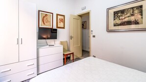 A bedroom with a bed, a TV on a dresser, a chair, and artwork on the walls. - Al Portico - In the Heart of Avola (Avola)