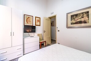 Ein Schlafzimmer mit einem Bett, einem Fernseher auf einer Kommode, einem Sessel und Kunstwerken an den Wänden.