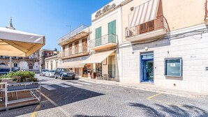 A street with buildings, a parked car, and a café with outdoor seating. - Al Portico - In the Heart of Avola (Avola)