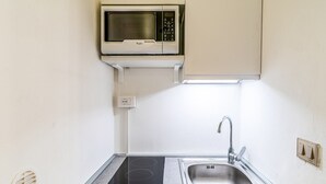 A compact kitchen with a microwave, an induction cooktop, a sink, and a power outlet. - Al Portico - In the Heart of Avola (Avola)