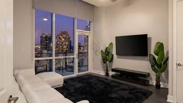 Una sala de estar moderna con un ventanal grande, un televisor de pantalla plana, un sofá y un tapete negro.
