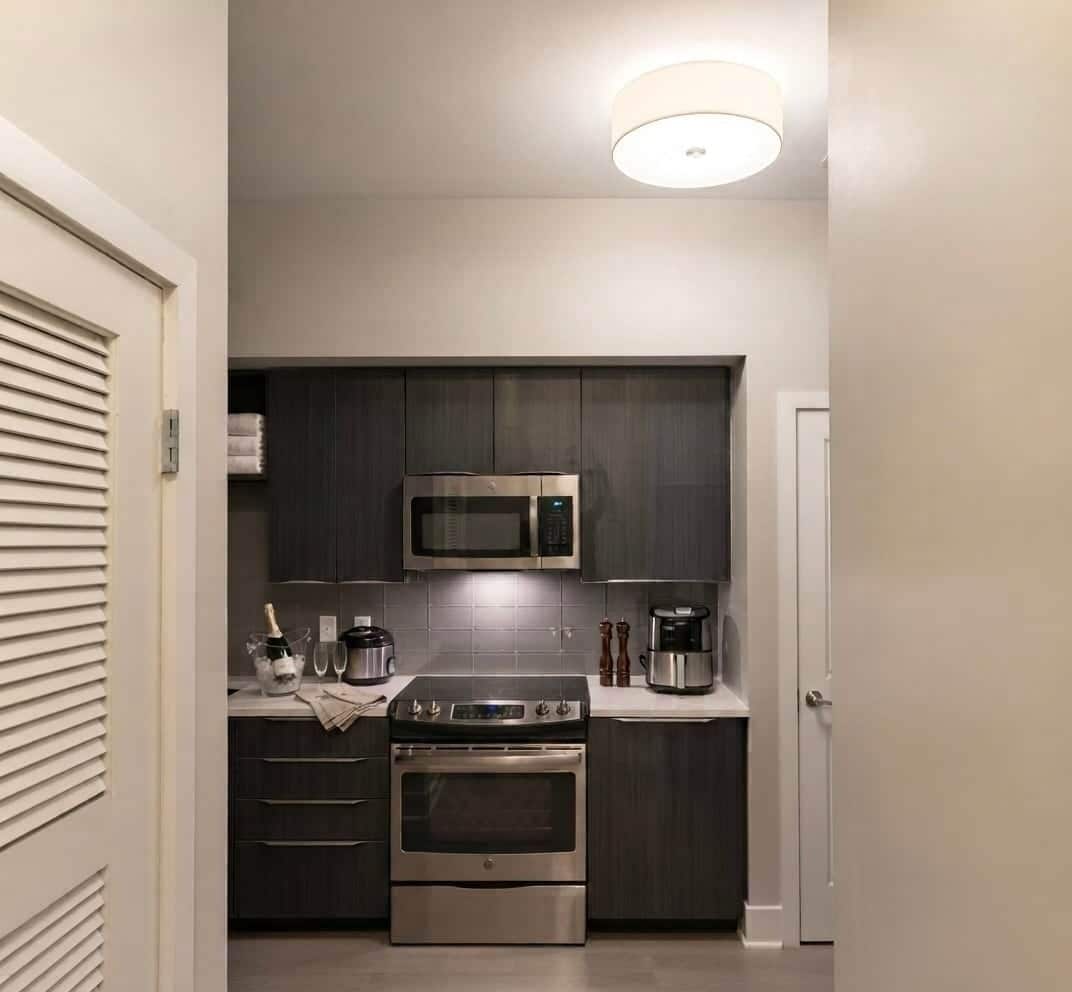 Una cocina compacta con muebles oscuros, un microondas de acero inoxidable, una cafetera y un horno empotrado.