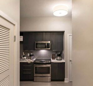 Una cocina compacta con muebles oscuros, un microondas de acero inoxidable, una cafetera y un horno empotrado.