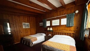 Una habitación estilo cabaña con dos camas, paredes de madera, una ventana con cortinas, un escritorio y una silla.