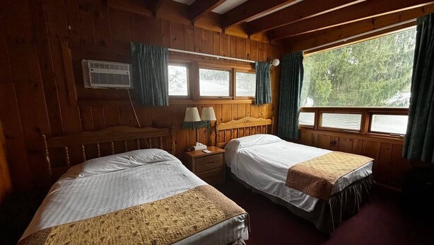 Una habitación con dos camas, cabecero de madera, ventana con cortinas y equipo de aire acondicionado.