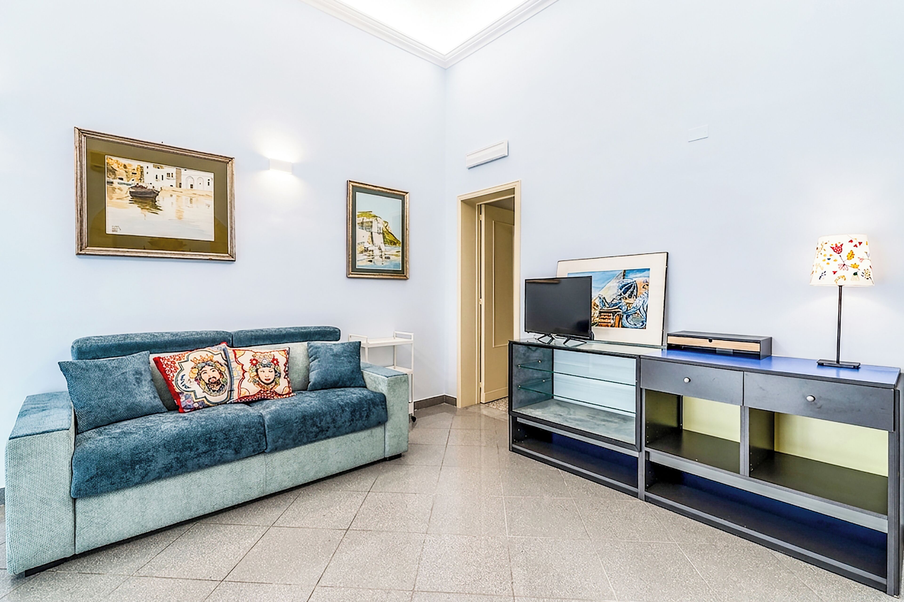A living room with a blue sofa, a TV, and framed artwork on the wall.