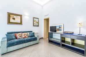 A living room with a blue sofa, a TV, and framed artwork on the wall. - Al Portico (Avola)