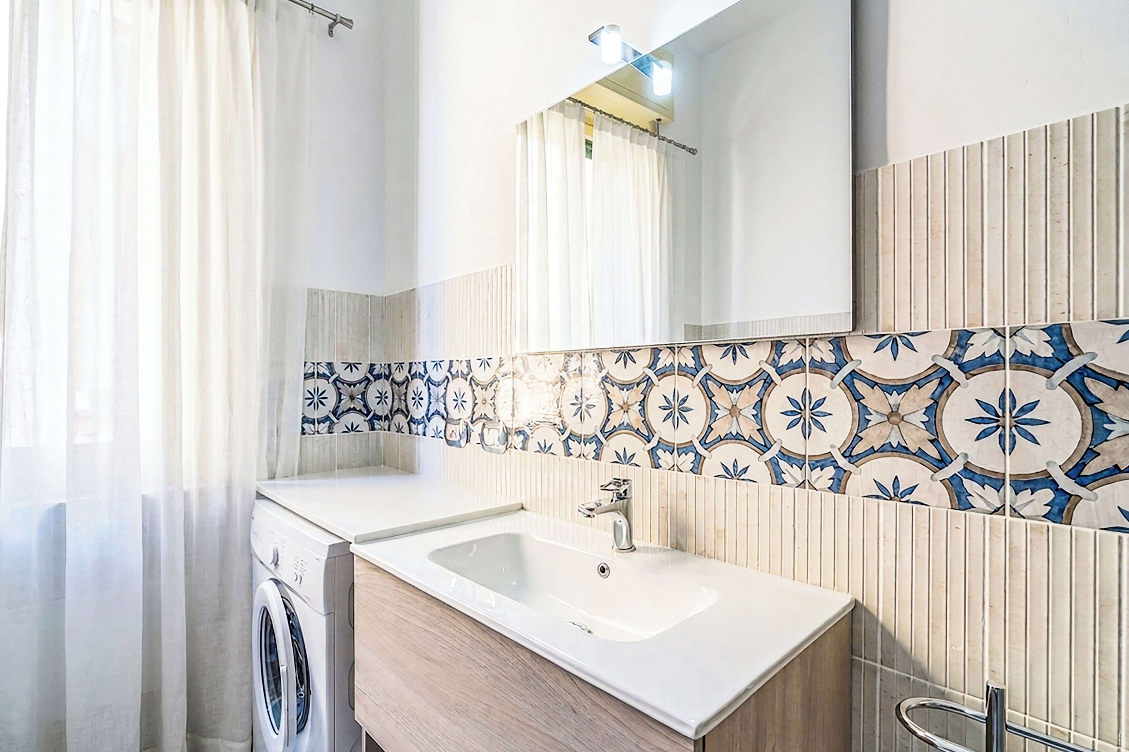 A bathroom with a washing machine, a sink, and a mirror.
