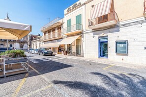 A street with buildings, a café with outdoor seating, and parked cars. - Al Portico (Avola)