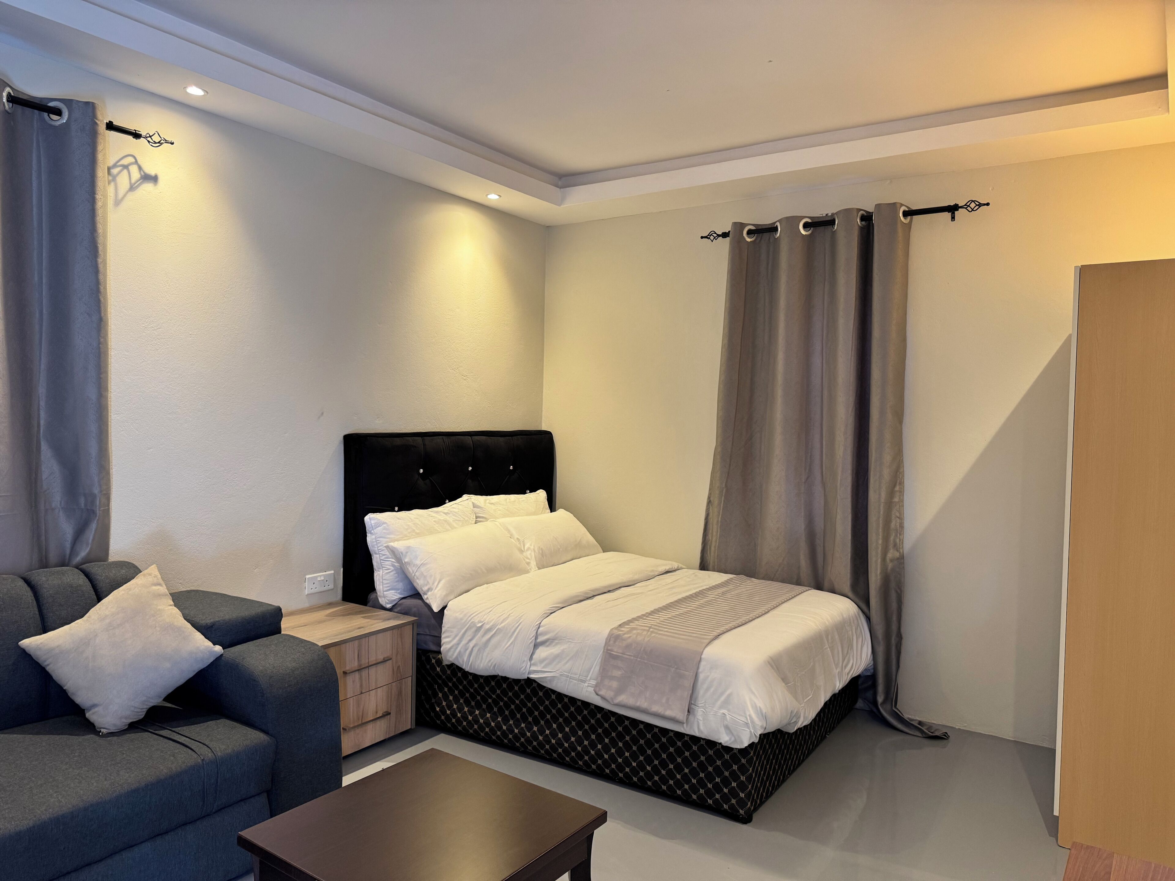 A bedroom with a bed, a nightstand, a sofa, and a wooden door.