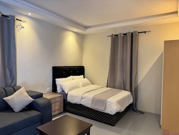 A bedroom with a bed, a nightstand, a sofa, and a wooden door.