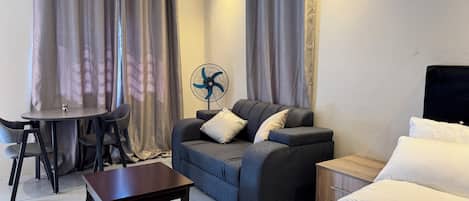 A modern hotel room with a sofa, a small table, a bed, and a fan.