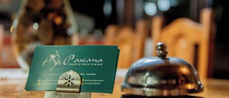 A business card for 'Pascana Cabana & Hosteria' with contact details, placed on a wooden table next to a metallic bell.
