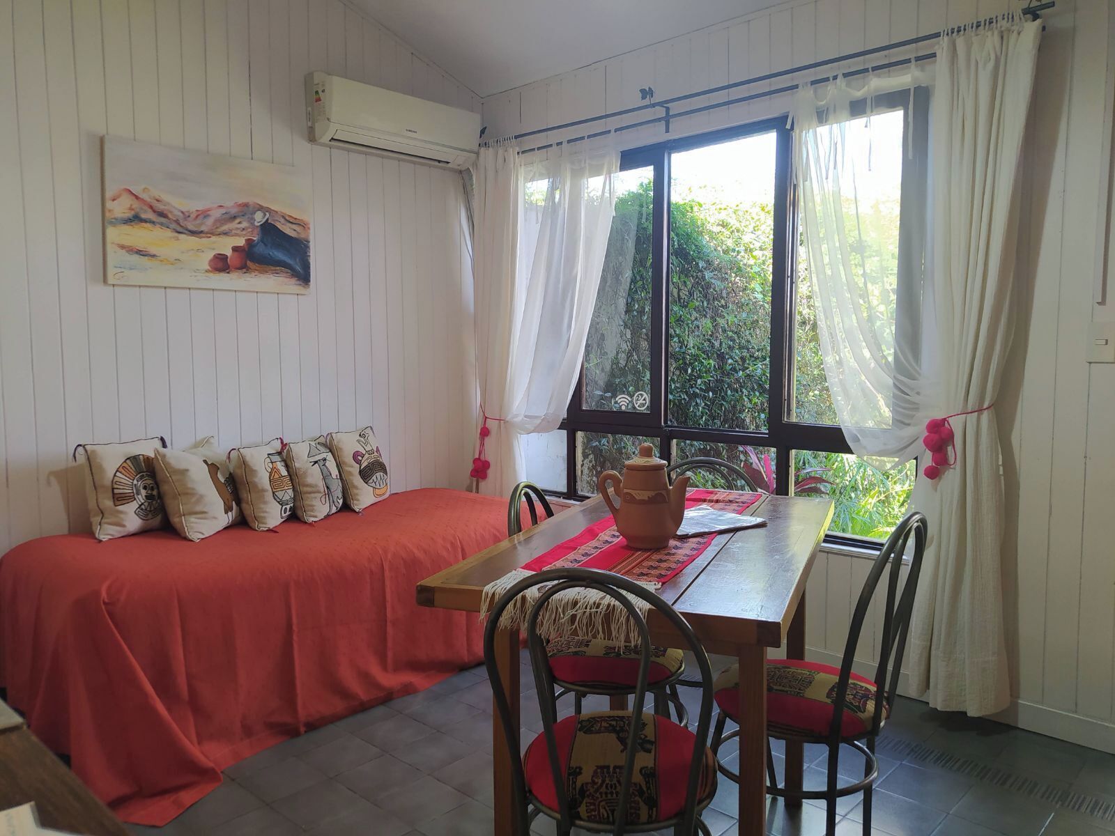 Una habitación con cama, una mesa, sillas y una ventana con cortinas.