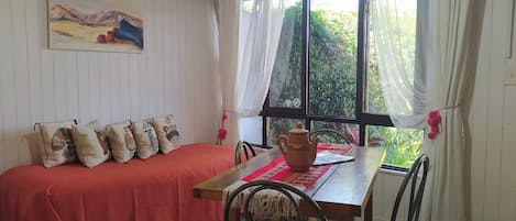 A room with a bed, a table, chairs, and a window with curtains.