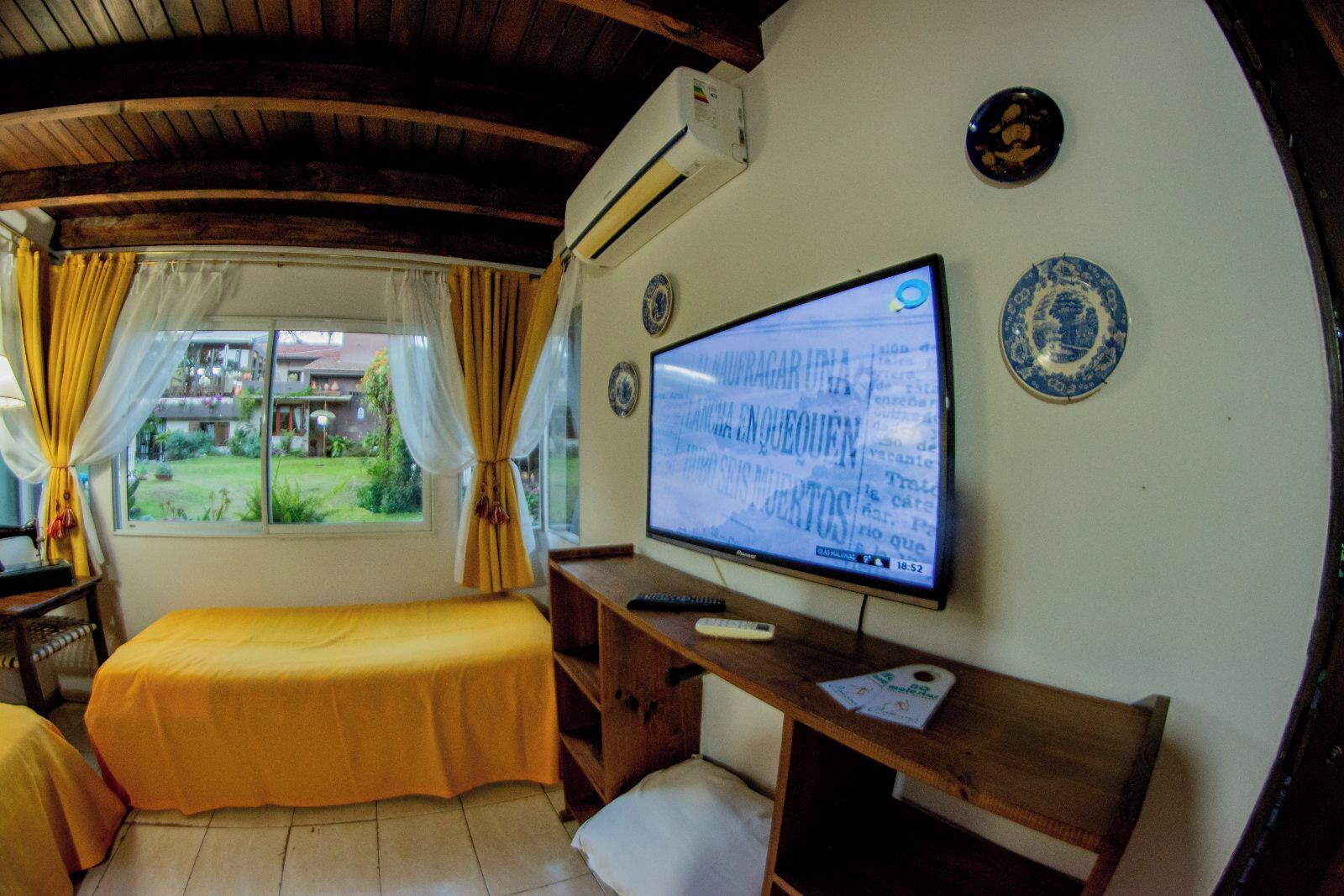 A room with a bed, a desk, a television, and a window with curtains.