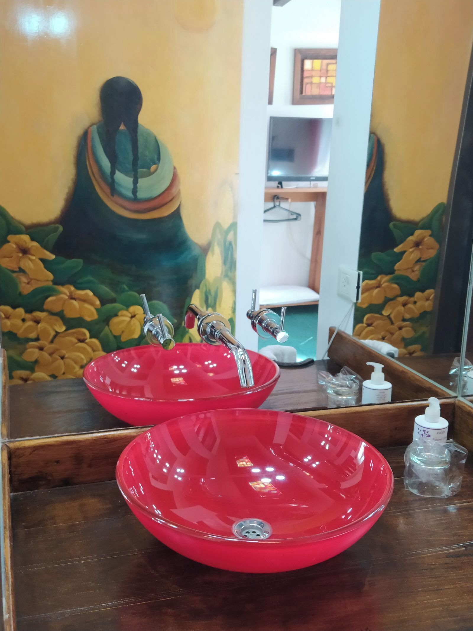 A bathroom with a large mirror, red sinks, and a wall painting.