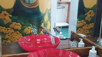 A bathroom with a large mirror, red sinks, and a wall painting.