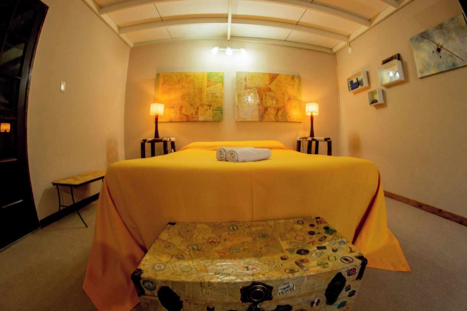 A hotel room with a bed, two wall-mounted lamps, a small table, and a suitcase.