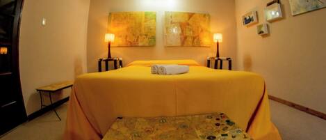 A hotel room with a bed, two wall-mounted lamps, a small table, and a suitcase.