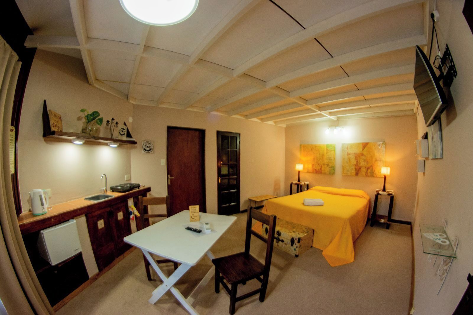 Una habitación pequeña con cama, una mesita, una silla, un escritorio con lavabo y un espejo.