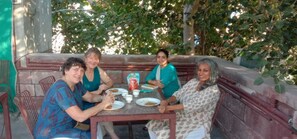 A group of people seated at an outdoor table with plates of food and cups, surrounded by greenery. - The Thikana Heritage  (Jodhpur)