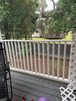 A wooden deck with a white railing, a black chair, and a purple object on the ground. - Enjoyable 2-bedroom condo with AC in charming Pensacola (Pensacola)