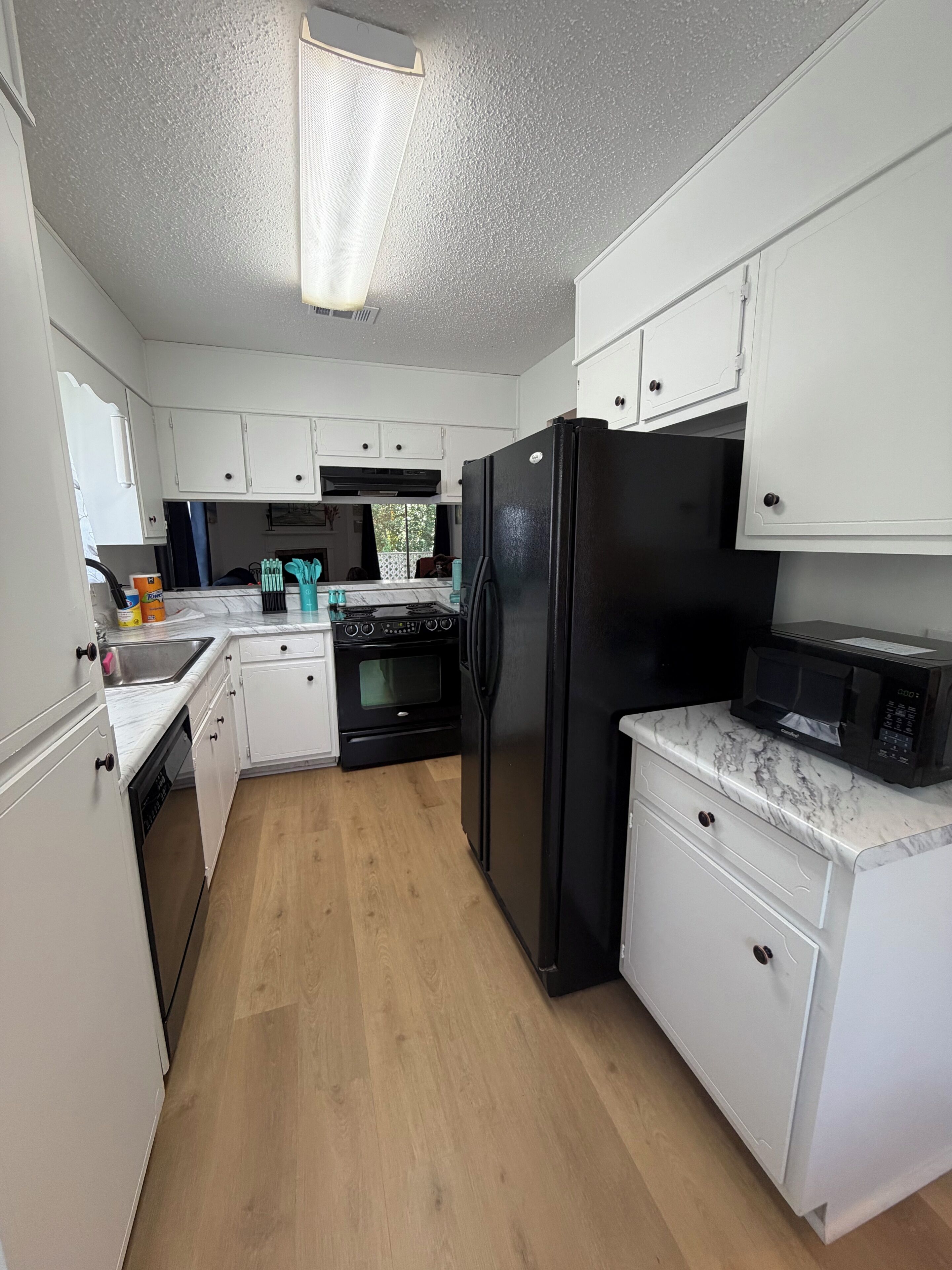 A kitchen with white cabinets, a black refrigerator, a microwave, and a stove.