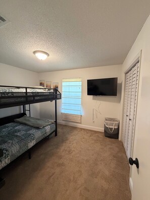 A room with bunk beds, a television, a window with blinds, and a door with a handle. - Enjoyable 2-bedroom condo with AC in charming Pensacola (Pensacola)