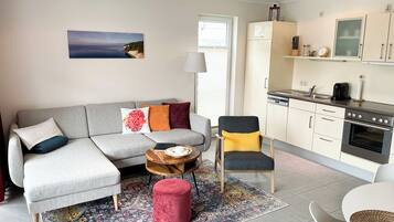 A modern living room with a grey sofa, a red ottoman, and a wooden coffee table.