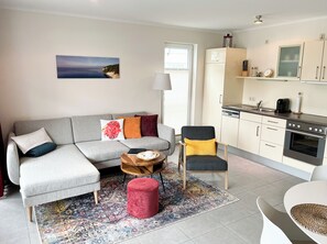 Un salon moderne avec un canapé gris, un pouf rouge et une table basse en bois.