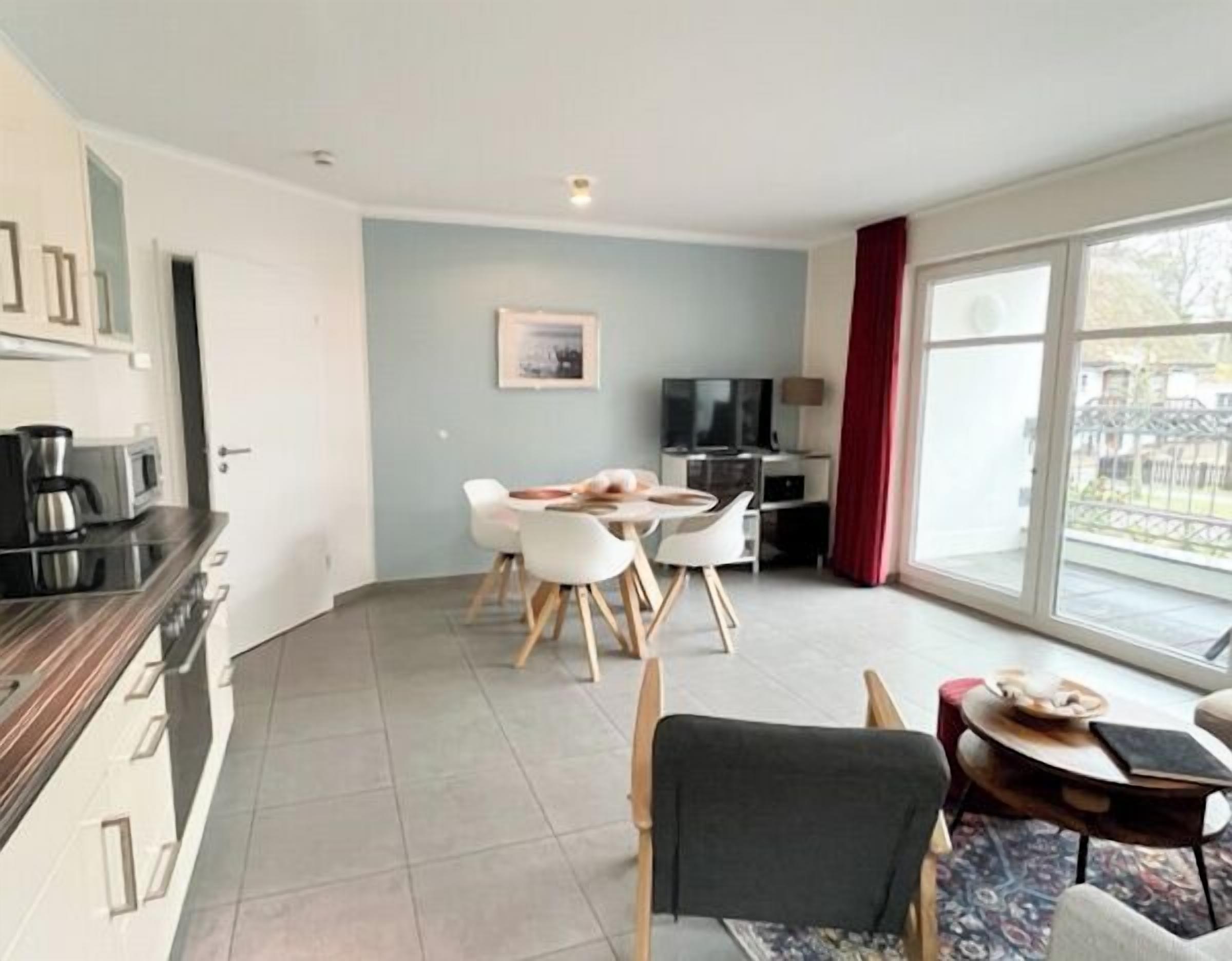 A modern living room with a dining area, a kitchen with appliances, and a large sliding glass door to the outside.