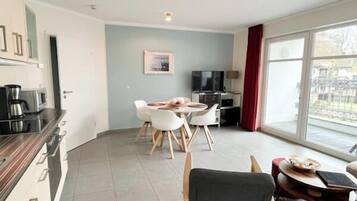 A modern living room with a dining area, a kitchen with appliances, and a large sliding glass door to the outside.