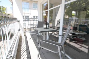 Un espace extérieur aménagé avec une table et des chaises, une cloison en verre et une vue sur la rue.
