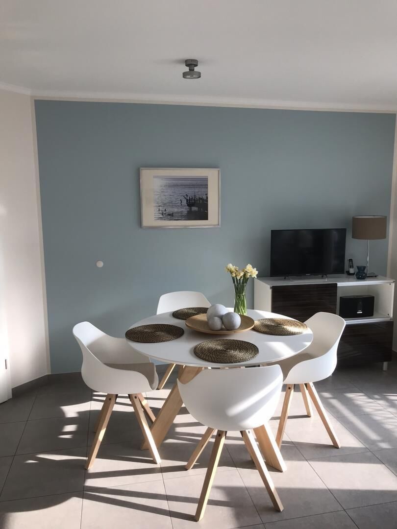 Un coin repas avec une table ronde, des chaises blanches et un téléviseur en arrière-plan.