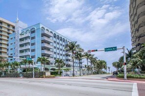 Un hôtel à plusieurs étages doté de balcons, un panneau de signalisation indiquant « Collins Ave », et des palmiers.