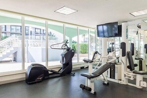 A gym with cardio equipment, weight machines, and a TV screen. - Miami Beach 2BR | Beachfront Pool Retreat (Surfside)