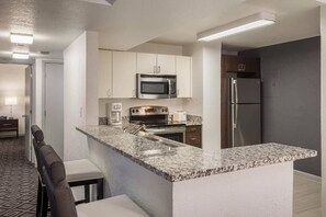A compact kitchen with a microwave, oven, and refrigerator, a granite countertop, and a seating area with a bench. - Miami Beach 2BR | Beachfront Pool Retreat (Surfside)