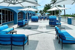 A poolside area with blue lounge chairs and umbrellas, a covered seating area, and a view of the ocean. - Miami Beach 2BR | Beachfront Pool Retreat (Surfside)