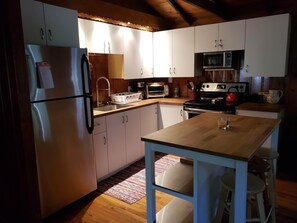 Une cuisine compacte équipée d’un réfrigérateur, d’un four à micro-ondes, d’une cuisinière et d’un évier. On y trouve une table en bois avec des tabourets, ainsi qu’un tapis à motifs sur le sol.