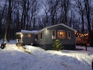 A two-story house with a covered porch, a deck, and a small tree in front. - Cozy 3-bedroom cabin in soothing Pocono Lake with AC, pools, lake, tennis court (Pocono lake)