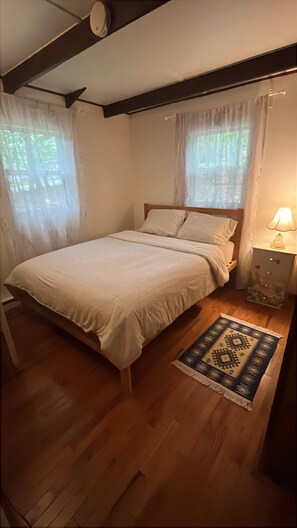 A bedroom with a bed, a nightstand with a lamp, and a patterned rug. - Cozy 3-bedroom cabin in soothing Pocono Lake with AC, pools, lake, tennis court (Pocono lake)