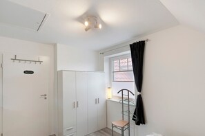 Una habitación con un armario blanco, una puerta con el letrero 'PRIVATE', una ventana con cortina y una silla.