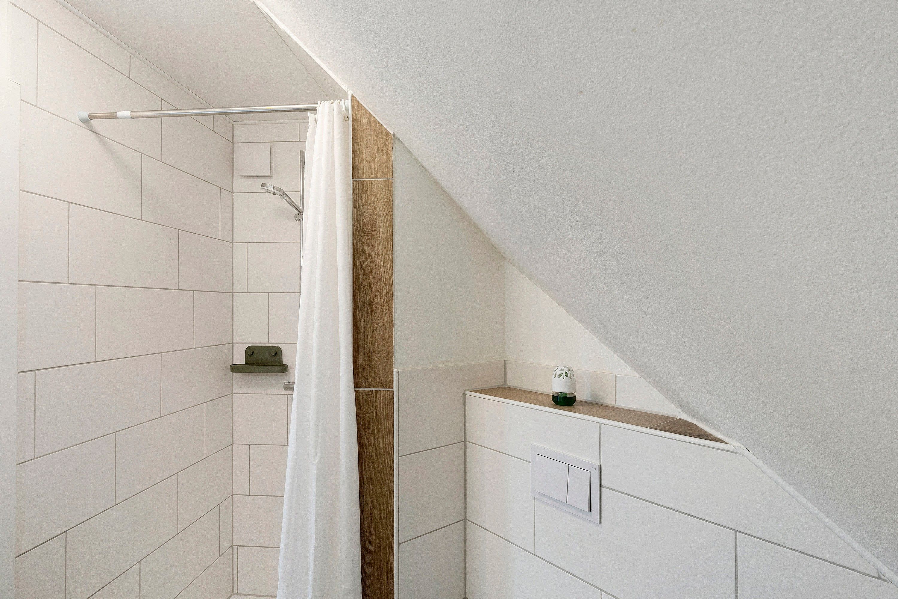 Un espace douche avec des carreaux blancs, un mur d’accent en bois et un rideau de douche blanc.