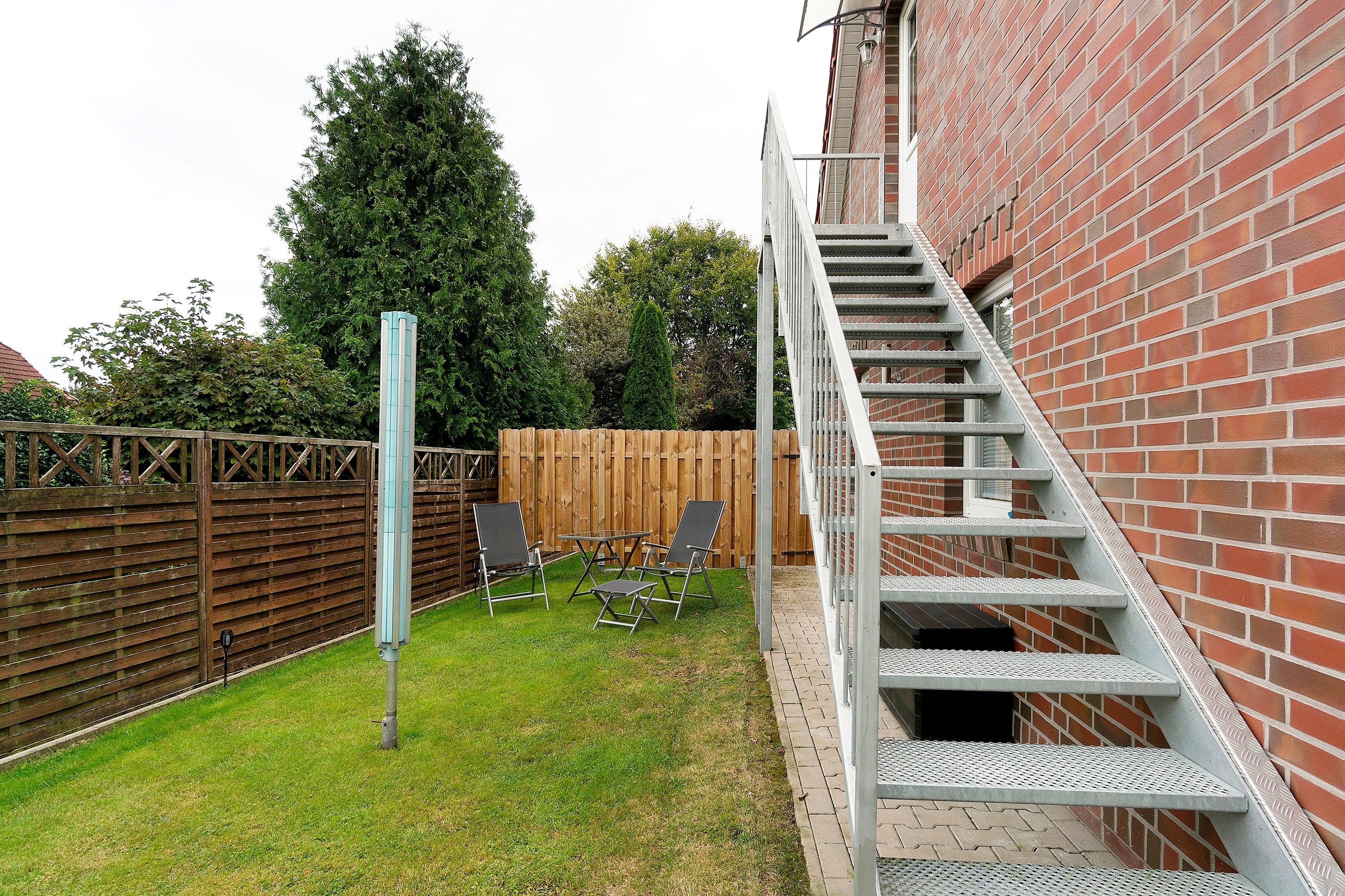 Ein Garten mit Holzzaun, Metalltreppe und Gartenmöbeln.